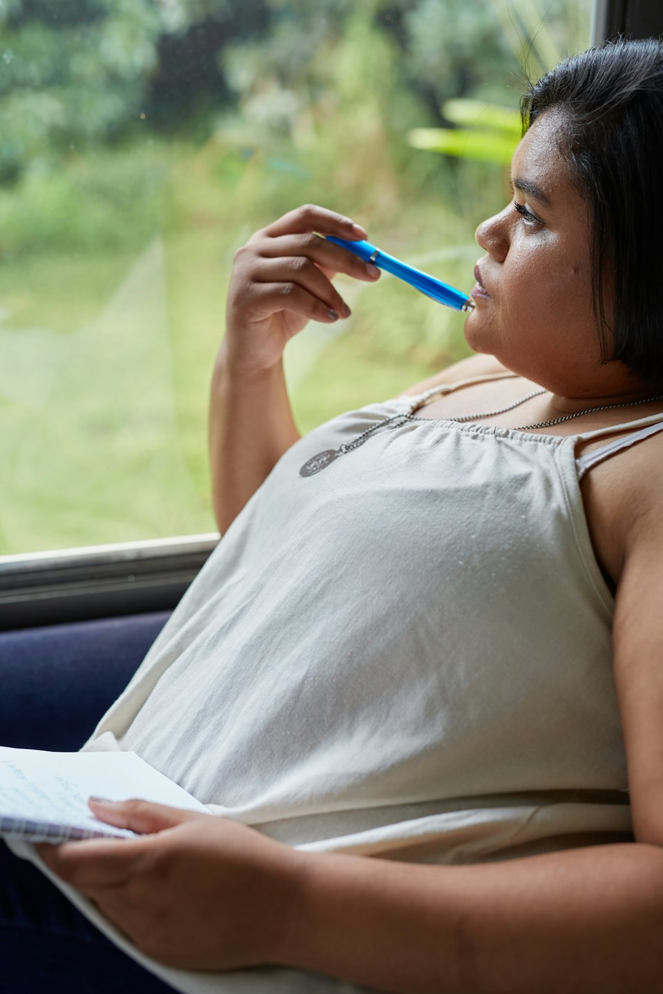 Woman contemplates with a pen to her lips and a notebook.