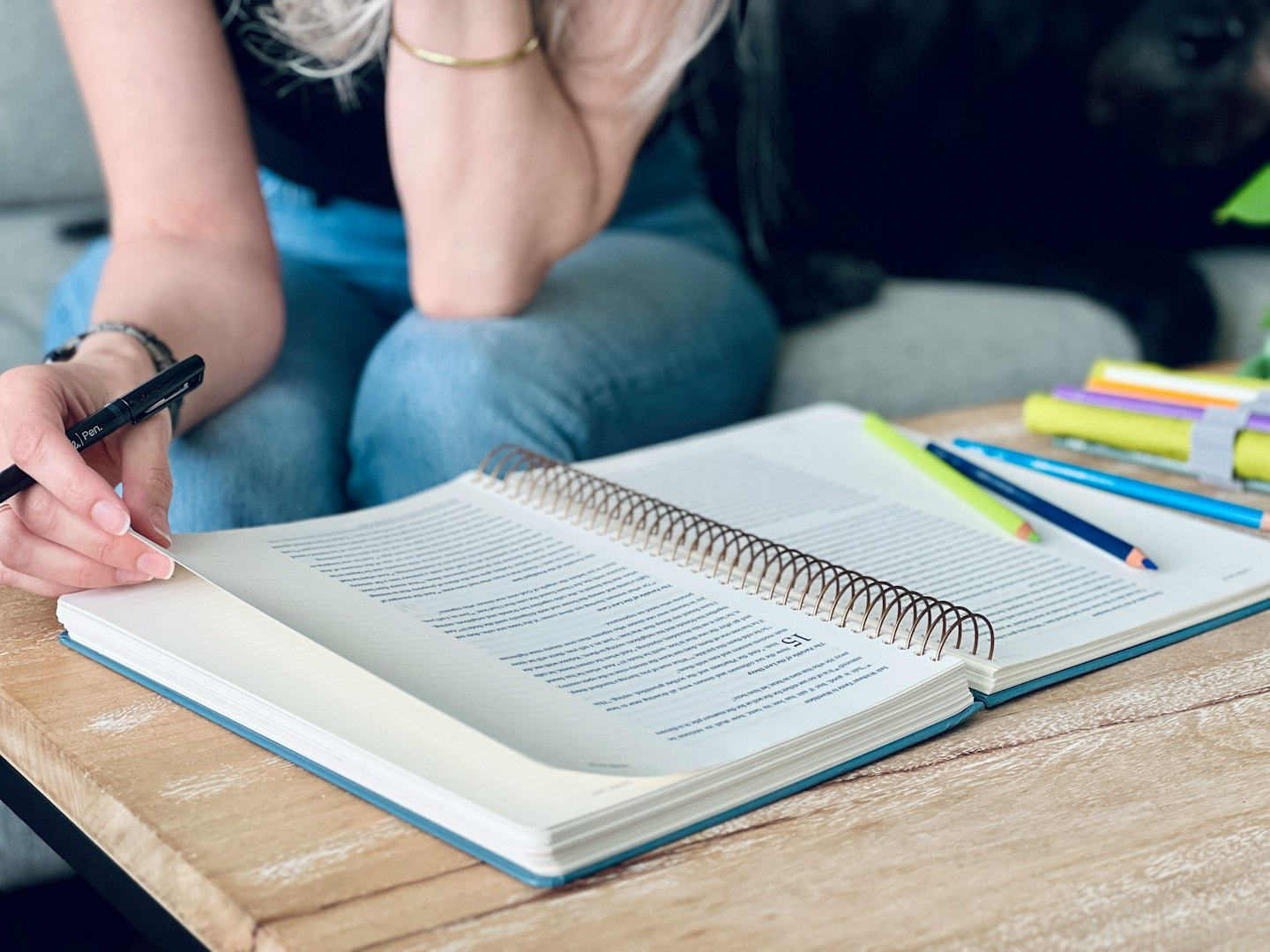 Person writing in a notebook at a wooden table.