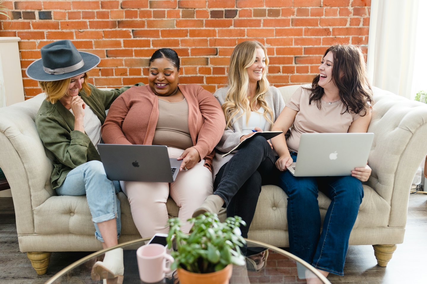 Diverse women collaborating on laptops on a sofa.