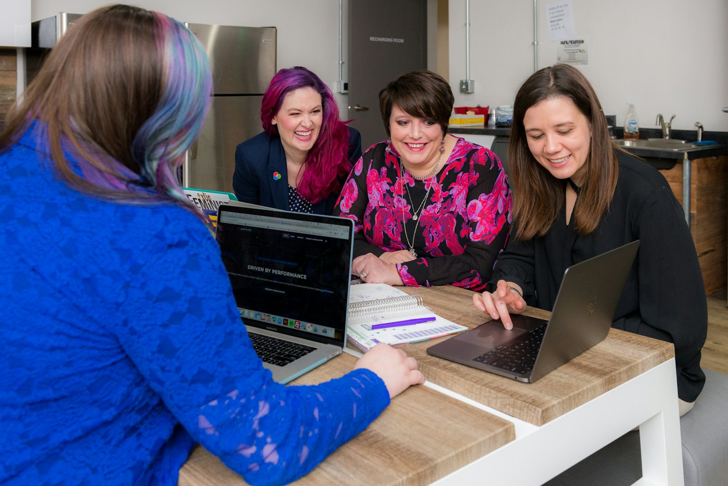 Diverse women coworkers collaborate and laugh in an office breakroom.