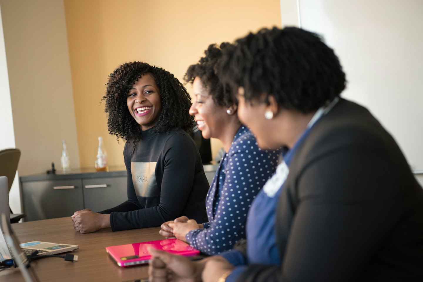 Three women collaborate and laugh at an office table.